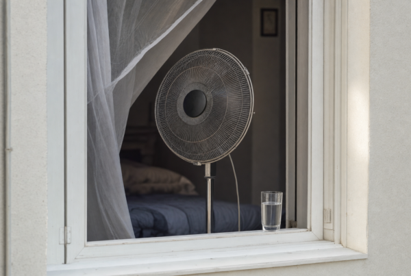Oscillating fan in front of open window with sheer curtain and water glass on sill