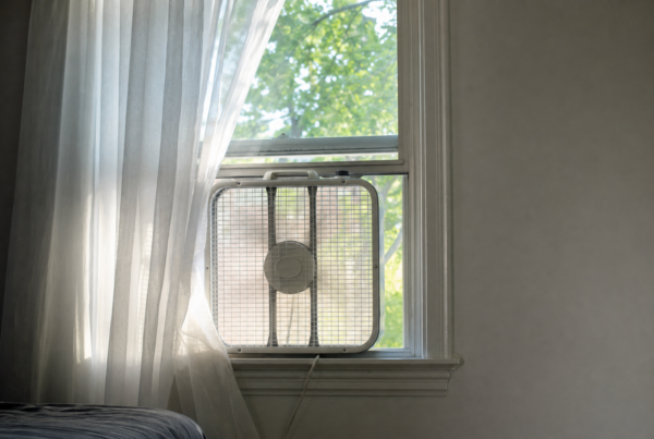 Window box fan in an open second-floor duplex window with sheer curtains and summer light